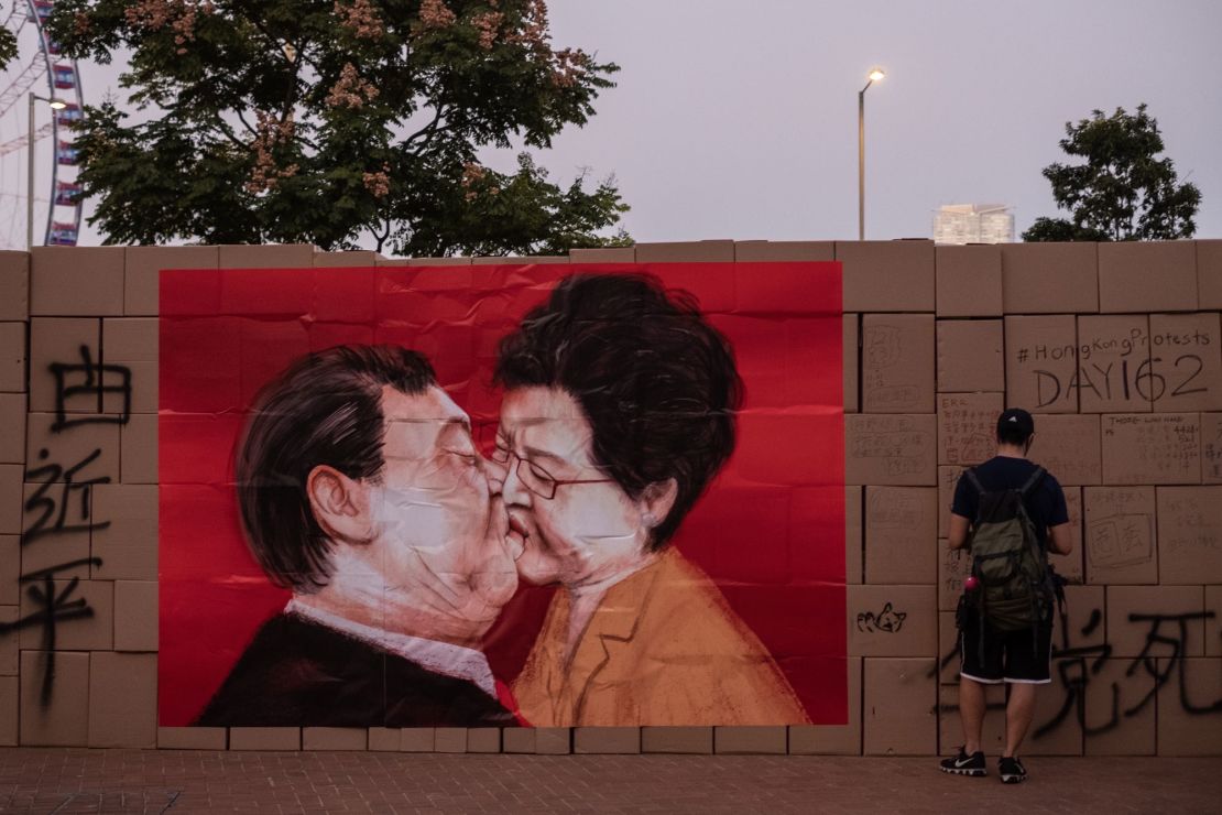 A demonstrator stands next to a poster featuring Chinese President Xi Jinping and Hong Kong Chief Executive Carrie Lam kissing, on a temporary wall built with cardboard boxes during a rally in the Central district of Hong Kong on November 17, 2019. 
