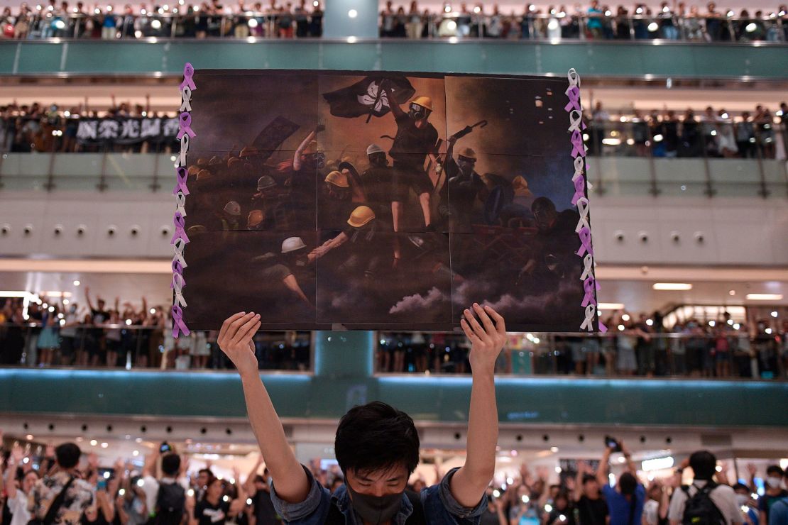 A man holds a poster aloft as protesters gather to sing "Glory to Hong Kong." The image is an adaption of 
"Liberty Leading the People" (1830) by Eugene Delacroix.