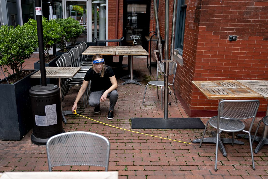 An employee wearing a protective shield uses a measuring tape to check the distance between tables and chairs in the outdoor seating area of a restaurant in Washington, D.C.