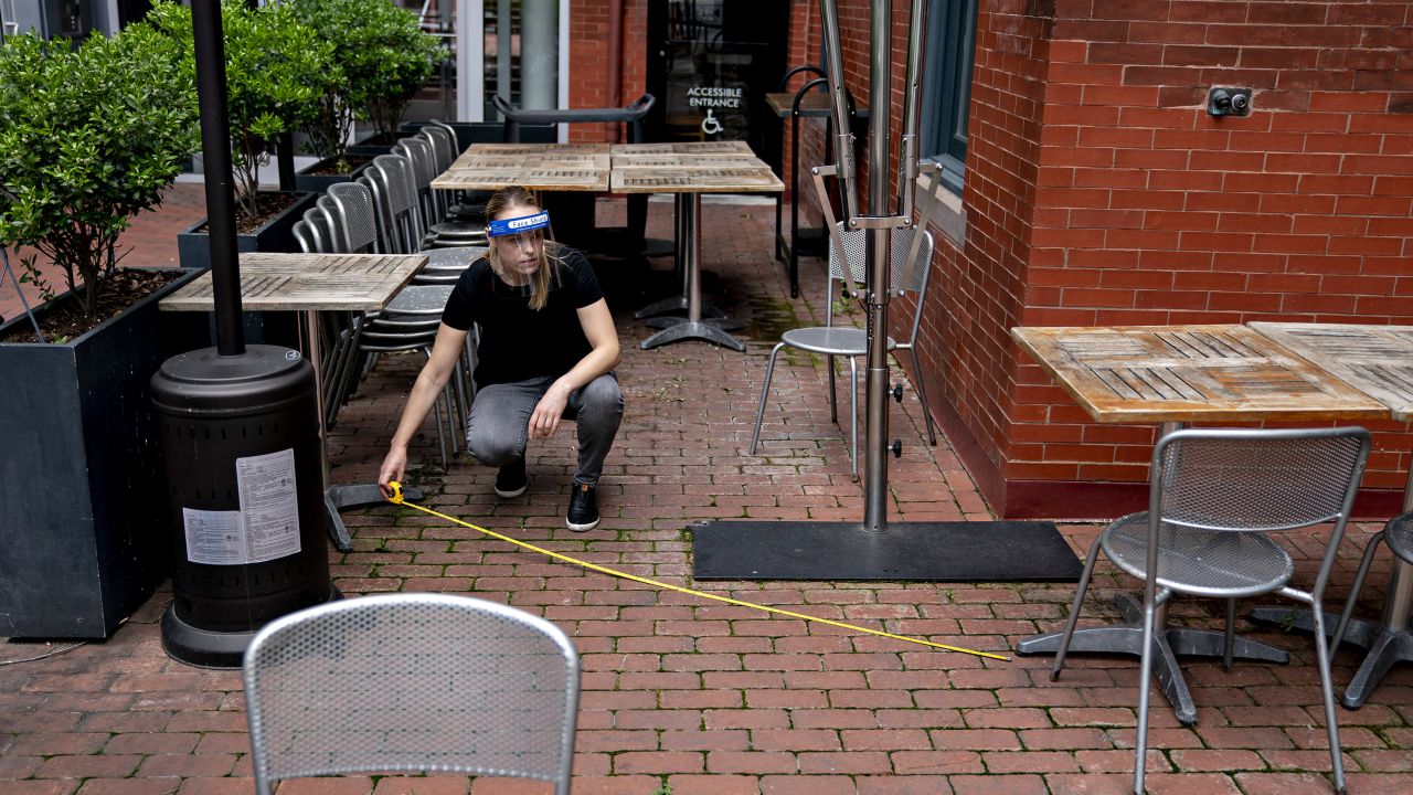 An employee wearing a protective shield uses a measuring tape to check the distance between tables and chairs in the outdoor seating area of a restaurant in Washington, D.C.