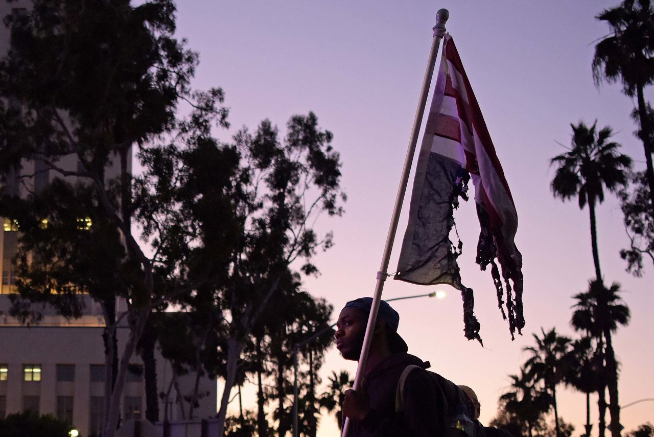 A man facing a row of police officers holds a burnt US flag as protesters gather in downtown Los Angeles on May 27.