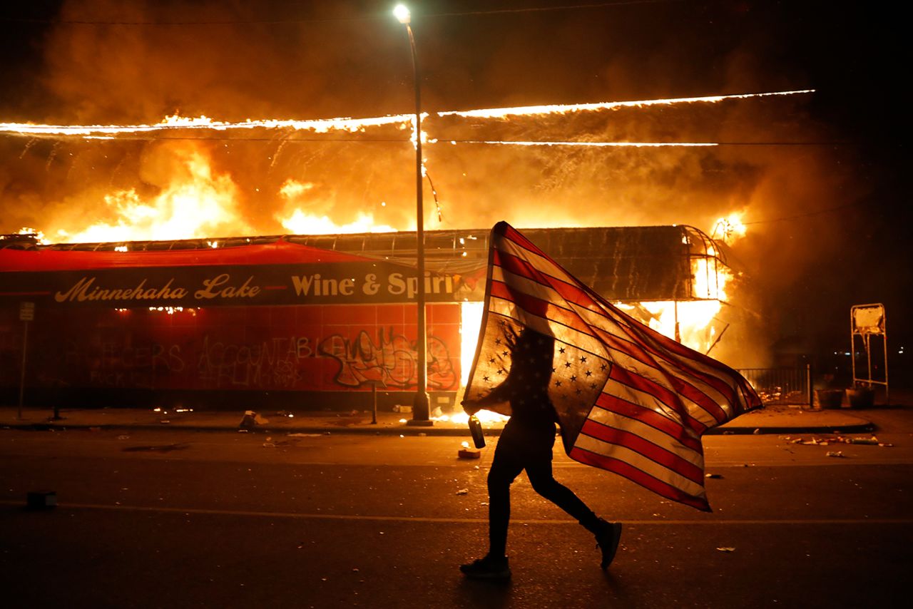 A protester carries an American flag upside down next to a burning building in Minneapolis on May 28.