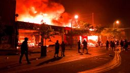 TOPSHOT - Flames rise from a liquor store and shops near the Third Police Precinct on May 28, 2020 in Minneapolis, Minnesota, during a protest over the death of George Floyd, an unarmed black man, who died after a police officer kneeled on his neck for several minutes. - A police precinct in Minnesota went up in flames late on May 28 in a third day of demonstrations as the so-called Twin Cities of Minneapolis and St. Paul seethed over the shocking police killing of a handcuffed black man. The precinct, which police had abandoned, burned after a group of protesters pushed through barriers around the building, breaking windows and chanting slogans. A much larger crowd demonstrated as the building went up in flames. (Photo by Kerem Yucel / AFP) (Photo by KEREM YUCEL/AFP via Getty Images)