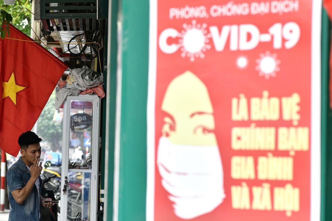 A propaganda poster on preventing the spread of the coronavirus is seen on a wall as a man smokes a cigarette along a street in Hanoi.