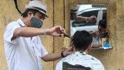 A roadside barber in Hanoi wearing a protective face mask in February of 2020 -- long before the US recommended face masks. (Photo by MANAN VATSYAYANA/AFP via Getty Images)