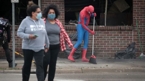 A person dressed as Spiderman sweeps the sidewalk as residents help clean up in Minneapolis.