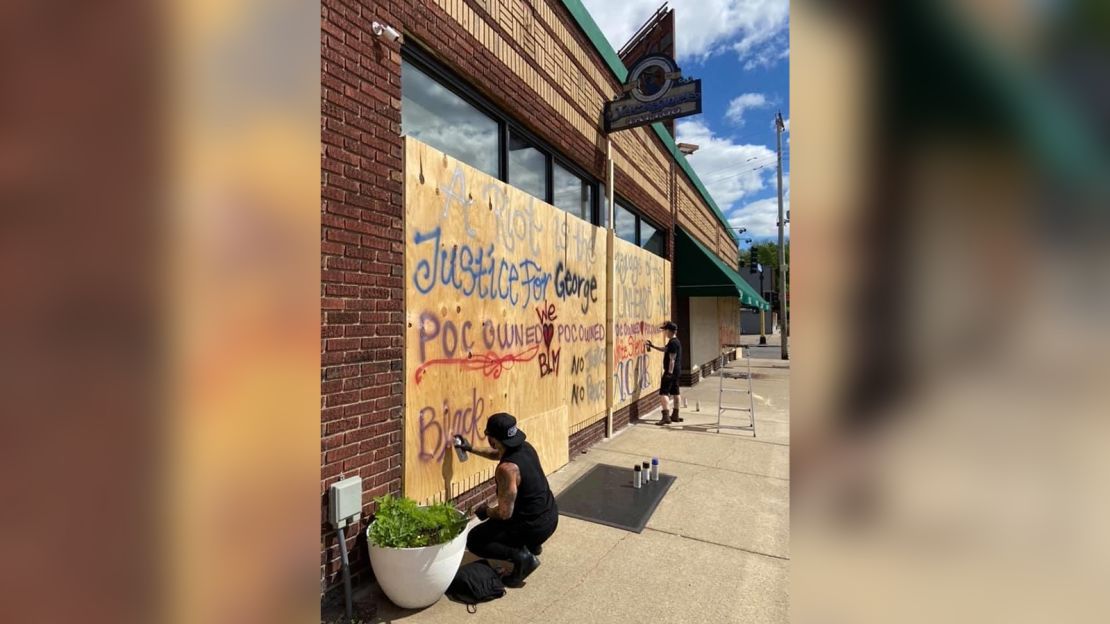 Emi Nijiya, left, and Amo Azure spray paint their tattoo parlor with slogans in support of protesters.