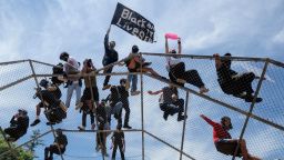People stand on top of a baseball backstop during a protest over the death of George Floyd in Los Angeles, Saturday, May 30, 2020. Protests across the country have escalated over the death of George Floyd who died after being restrained by Minneapolis police officers on Memorial Day, May 25.