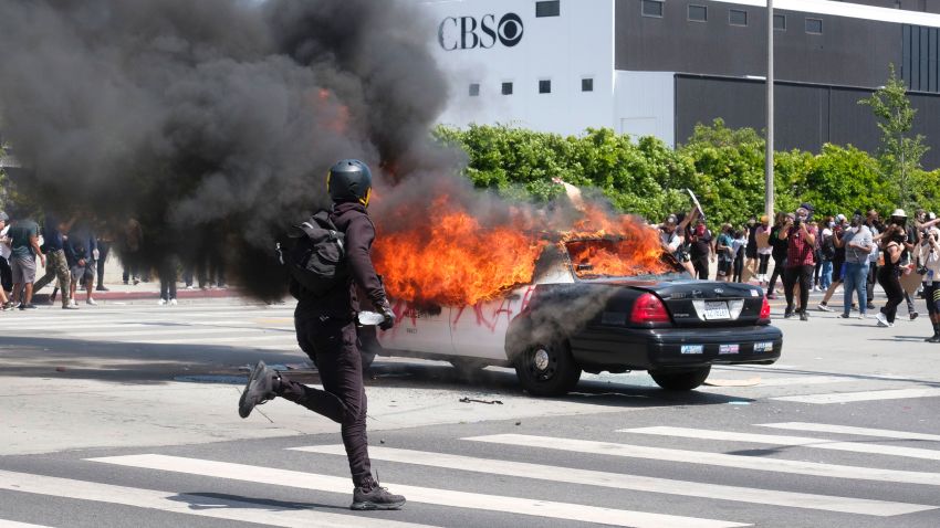 A person runs while a police vehicle is burning during a protest over the death of George Floyd in Los Angeles, Saturday, May 30, 2020. Protests across the country have escalated over the death of George Floyd who died after being restrained by Minneapolis police officers on Memorial Day, May 25.