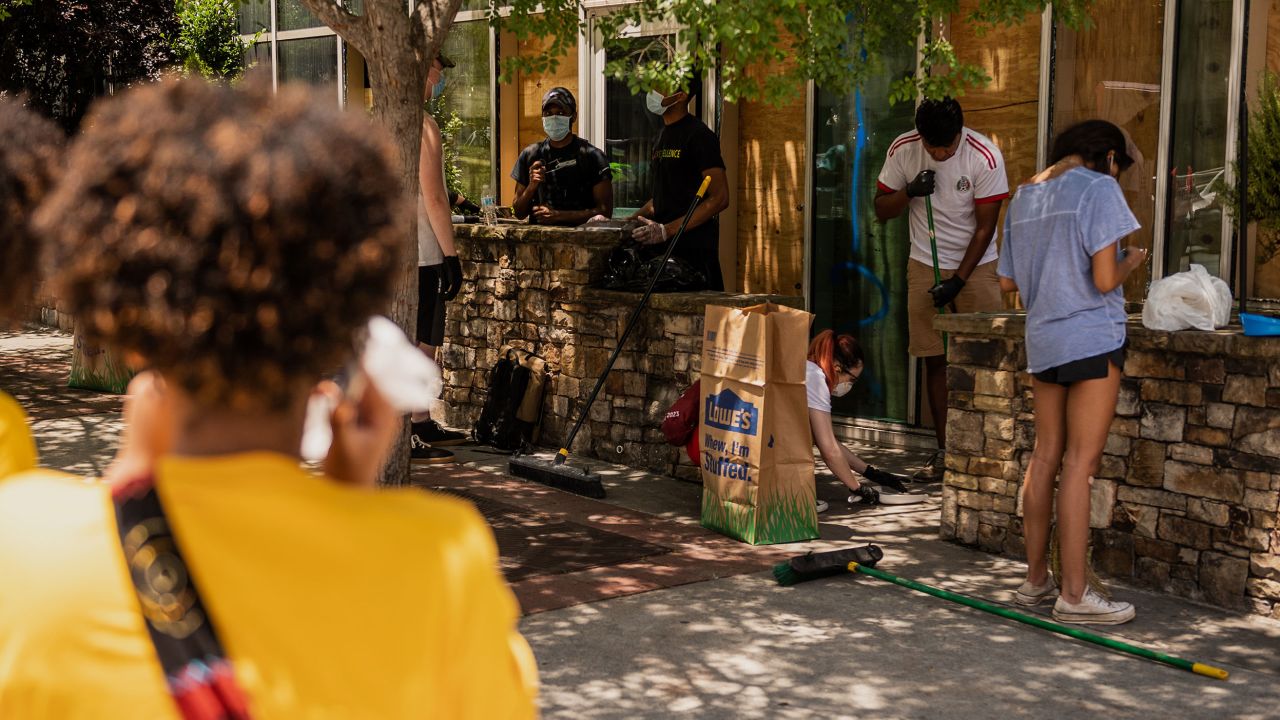 People clean up broken glass and debris outside McCormick & Schmick's restaurant in downtown Atlanta, Georgia, on Saturday, May 30. The building was vandalized during Friday night's protests over the death of George Floyd.