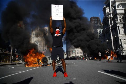 A protester holds a sign while a vehicle burns in a Philadelphia street on May 30.