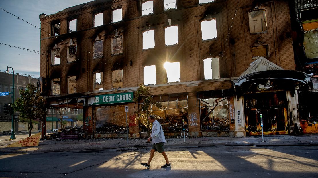 A man walks past a damaged building following overnight protests over the death of George Floyd, Sunday, May 31, 2020, in Minneapolis.