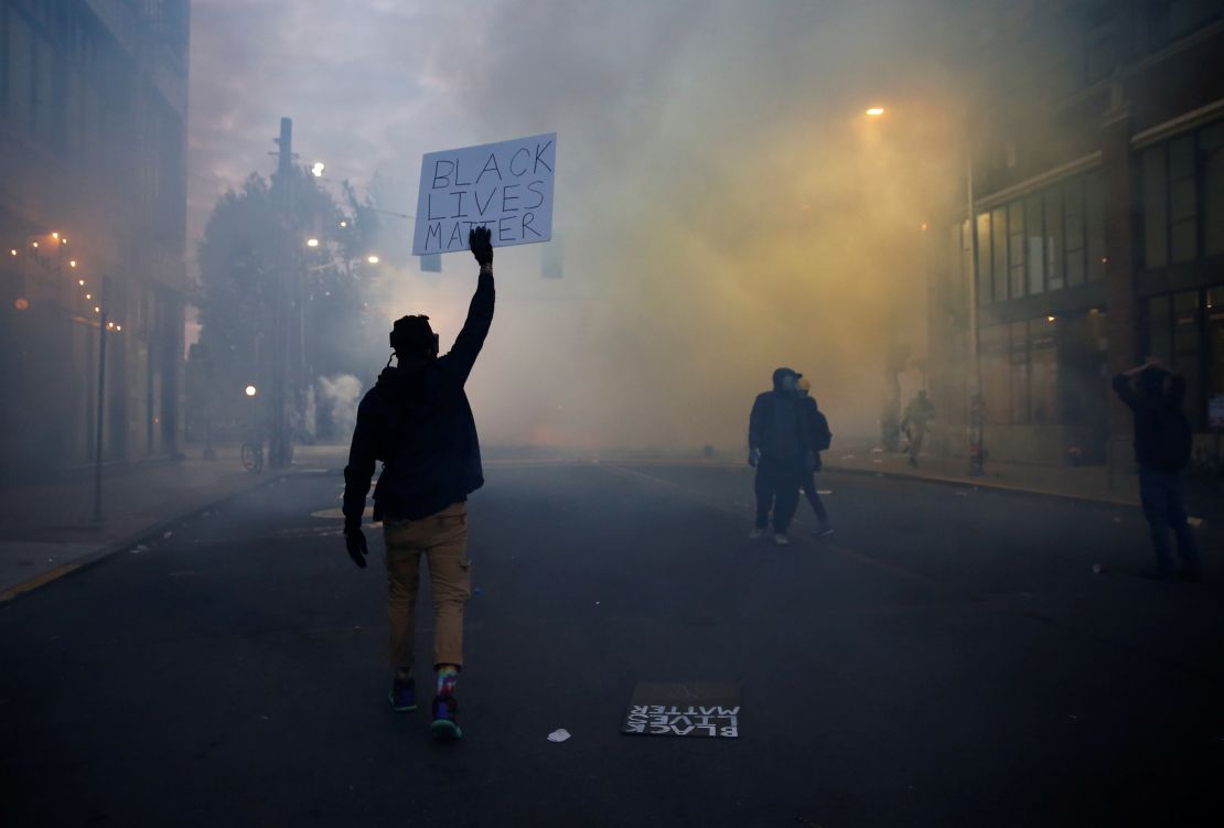 A person holds a "Black Lives Matter" sign as as a heavy cloud of tear gas and smoke rises after being deployed by Seattle police on June 1.