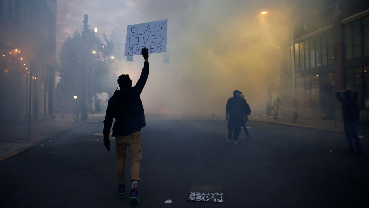A person holds a "Black Lives Matter" sign as as a heavy cloud of tear gas and smoke rises after being deployed by Seattle police on June 1.
