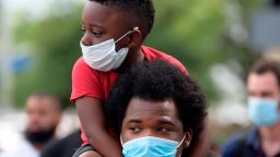 A young boy sits on the shoulder's of a man, both wearing facemasks, during a "Justice for George Floyd" event in Houston, Texas on May 30, 2020, after George Floyd, an unarmed black, died while being arrested and pinned to the ground by a Minneapolis police officer. - Clashes broke out and major cities imposed curfews as America began another night of unrest Saturday with angry demonstrators ignoring warnings from President Donald Trump that his government would stop violent protests over police brutality "cold." (Photo by Mark Felix / AFP) (Photo by MARK FELIX/AFP via Getty Images)