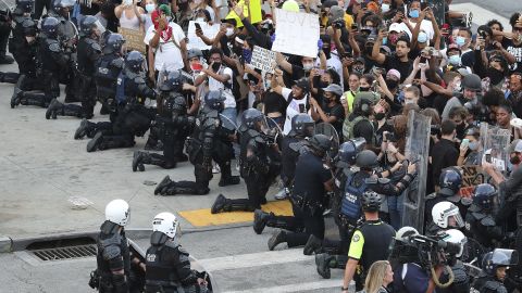 In a show of peace and solidarity, law enforcement officials with riot shields take a knee in front of protesters on Monday, June 1, 2020, in Atlanta
