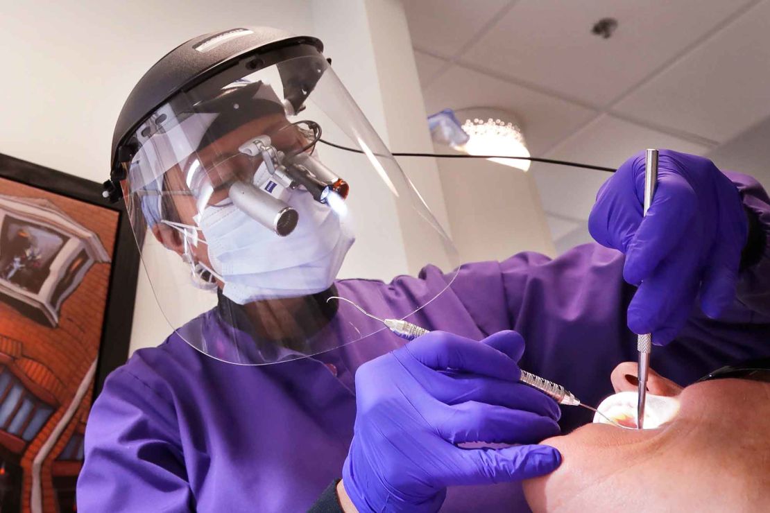 Dentist Dr. Kathleen Saturay wears additional protective equipment, including a face shield and disposable mask over a respirator mask, as she works with a patient in Seattle.