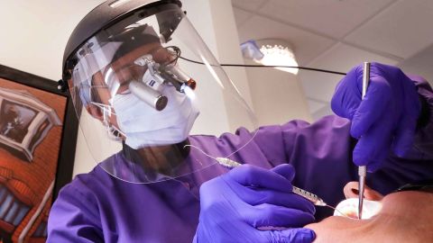 Dentist Dr. Kathleen Saturay wears additional protective equipment, including a face shield and disposable mask over a respirator mask, as she works with a patient in Seattle.