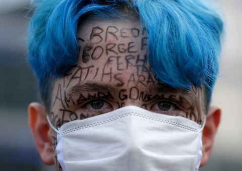 A man attending a demonstration in Berlin, with the names of victims of police violence written on his face.