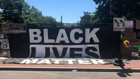 A large Black Lives Matter flag hangs from the fence, with the Washington Monument spotted in the background.