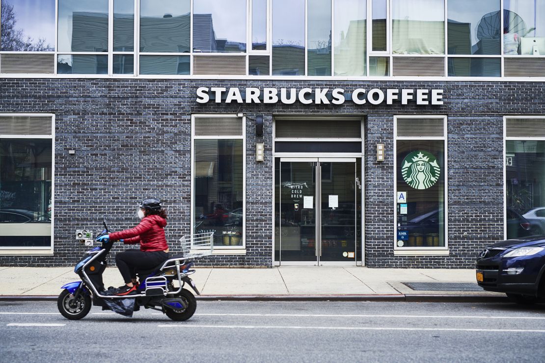A person wearing a protective mask rides a scooter past a temporarily closed Starbucks coffeeshop in Brooklyn, NY, on April 27, 2020.