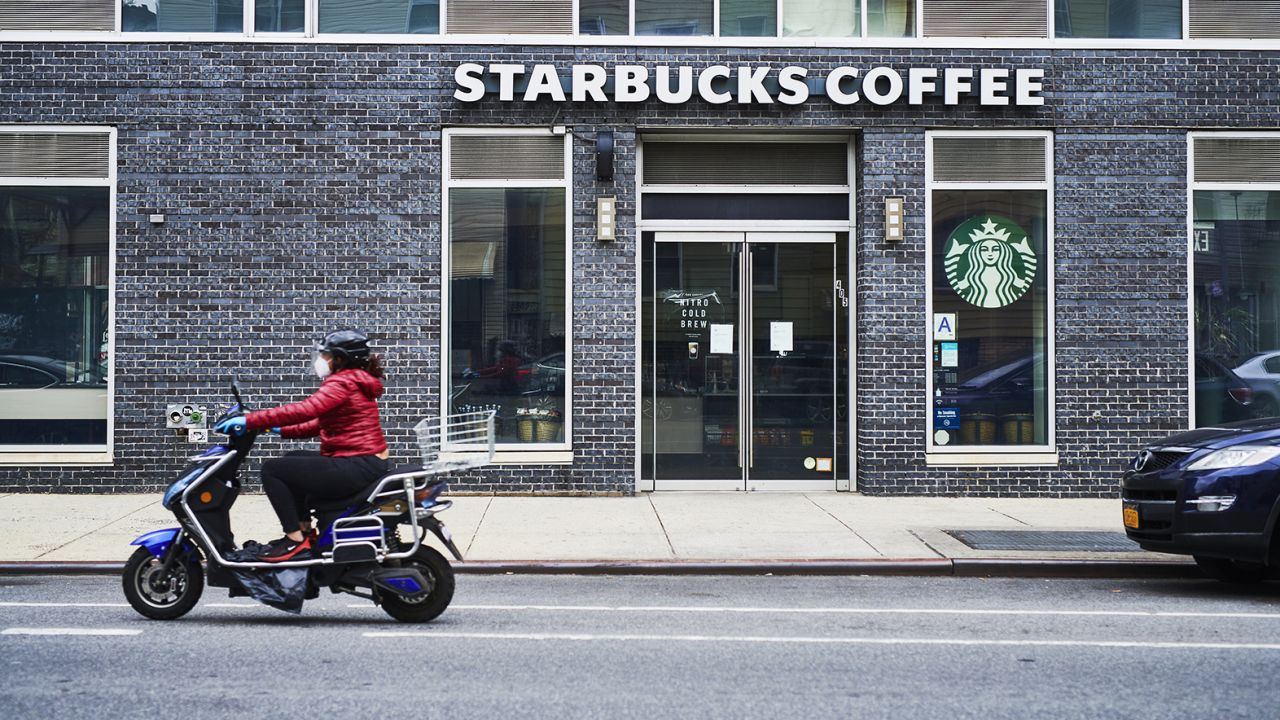 A person wearing a protective mask rides a scooter past a temporarily closed Starbucks coffeeshop in Brooklyn, NY, on April 27, 2020.