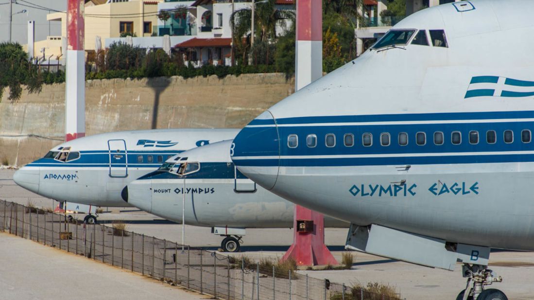 <strong>Olympic Airways:</strong> A small fleet of decommissioned Boeing aircraft, including an imposing 747-200 alongside a Boeing 737 and Boeing 727, sit idle on the edge of the complex.