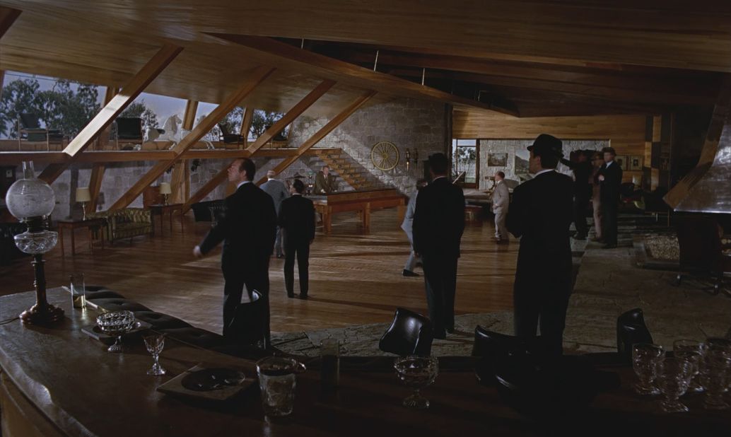 <strong>The Rumpus Room, "Goldfinger" (1964) -- </strong>The Rumpus Room at Auric Goldfinger's Kentucky stud farm owed a debt Frank Lloyd Wright with Adam's choice of straight lines and warm, polished wood alongside cold stone. (Incidentally, Goldfinger was supposedly named after modernist architect Erno Goldfinger, <a href="https://www.theguardian.com/uk/2005/jun/03/film.hayfestival2005" target="_blank" target="_blank">who Fleming reportedly took a dim view of</a>.)  <br /><br />As a space, the Rumpus Room was villainy at its most ergonomic. A control panel beneath a pool table operated the room: A wall becomes a map of Fort Knox and a floor compartment contained a model of the facility and its grounds. More importantly, the room's large windows and huge fireplace could be sealed off turn the space into a gas chamber to off rival gangsters. 