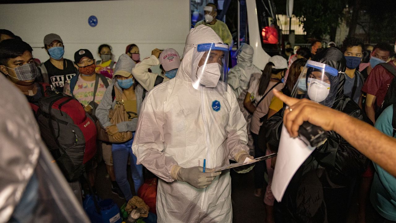 Workers in protective suits are seen as Filipinos out of work and stranded due to the coronavirus pandemic queue to take a free bus ride home to their province on May 29, 2020 in Paranaque, Metro Manila.