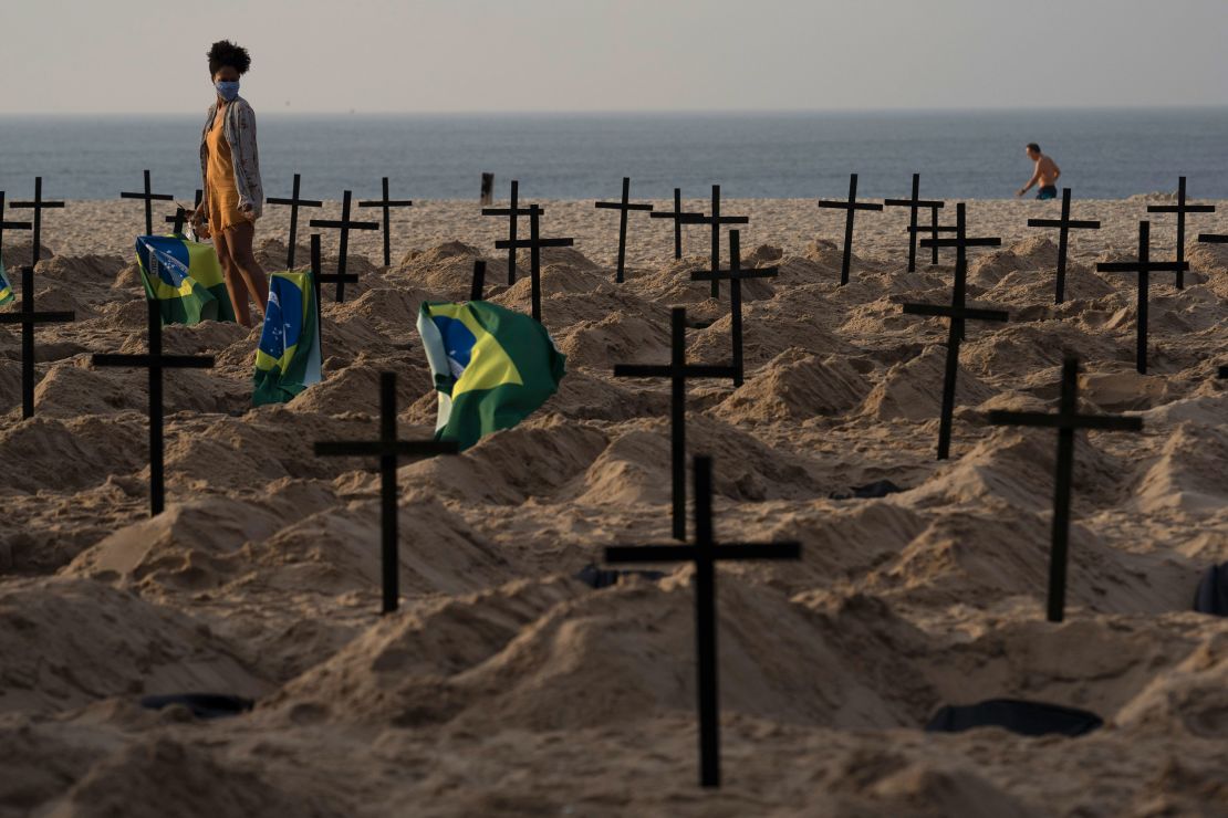 A woman walks amid symbolic graves on Rio de Janeiro's Copacabana beach. They were dug by activists protesting the government's handling of the Covid-19 pandemic.