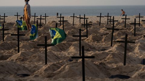 A woman walks amid symbolic graves on Rio de Janeiro's Copacabana beach. They were dug by activists protesting the government's handling of the Covid-19 pandemic.