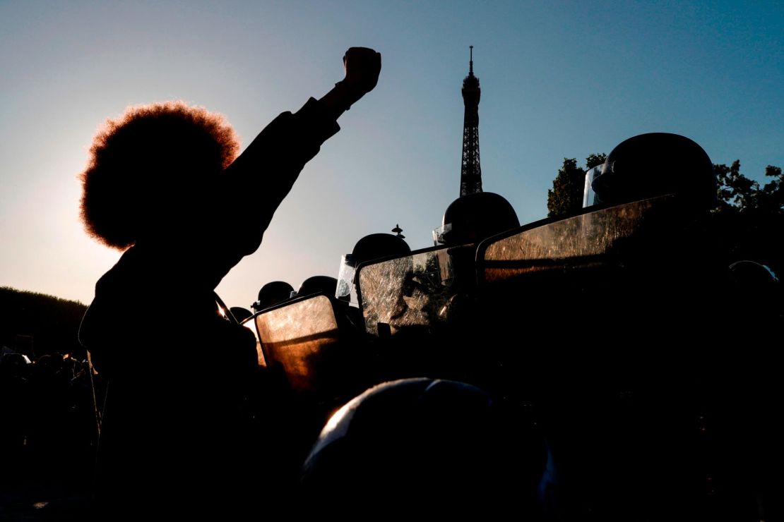 People raise their fists in front of riot policemen during a protest at the Champ de Mars in Paris, with the Eiffel Tower in the background as part of worldwide "Black Lives Matter" protests in the wake of the death of George Floyd,