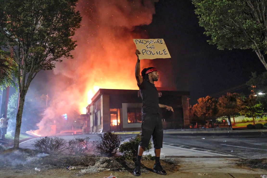 A person holds a sign as a Wendy's restaurant burns Saturday in Atlanta