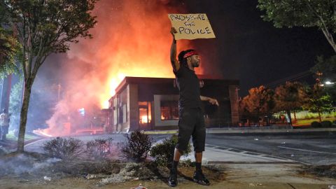 A person holds a sign as a Wendy's restaurant burns Saturday in Atlanta