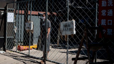 A woman stands behind a fence as she waits for the delivery of goods she ordered online in a residential area under lockdown near the closed Xinfadi market in Beijing.