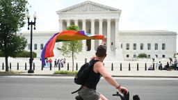 A man waves a rainbow flag as he rides by the US Supreme Court that released a decision that says federal law protects LGBTQ workers from discrimination on June 15, 2020 in Washington.