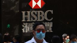 Pedestrians wear face masks as they walk past HSBC signage outside a branch of the bank in Hong Kong on April 28, 2020. - HSBC on April 28 said first quarter pre-tax profits almost halved as the banking giant was battered by the global coronavirus pandemic while it embarked on a major restructuring. (Photo by Anthony WALLACE / AFP) (Photo by ANTHONY WALLACE/AFP via Getty Images)