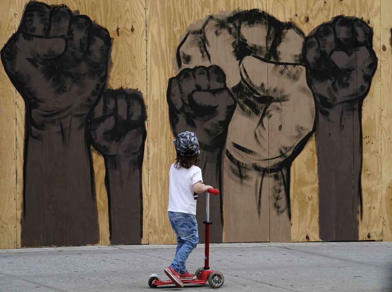A child rides a scooter past a mural by artists Malik Crawford and Jerome Tiunayan on a boarded-up store in New York on June 15.