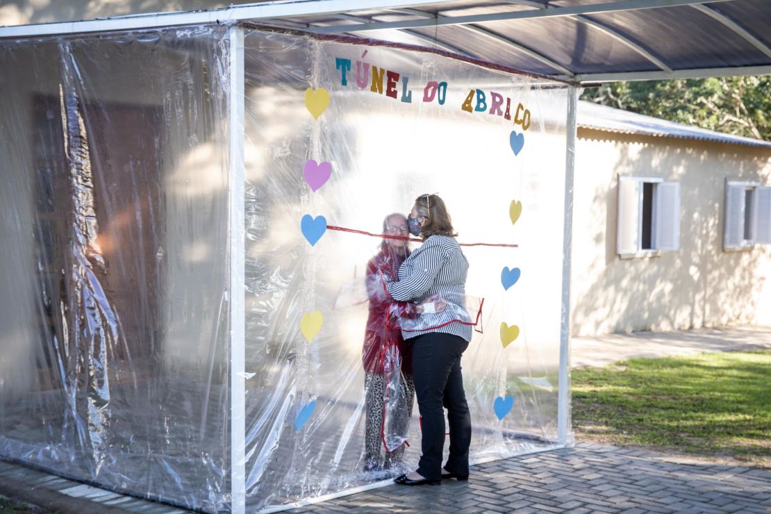 A daughter and mother embrace through the thick plastic curtain and sleeves of the "hug tunnel."