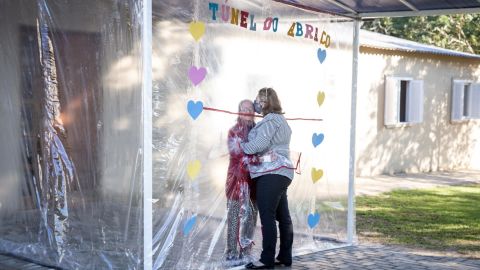A daughter and mother embrace through the thick plastic curtain and sleeves of the "hug tunnel."