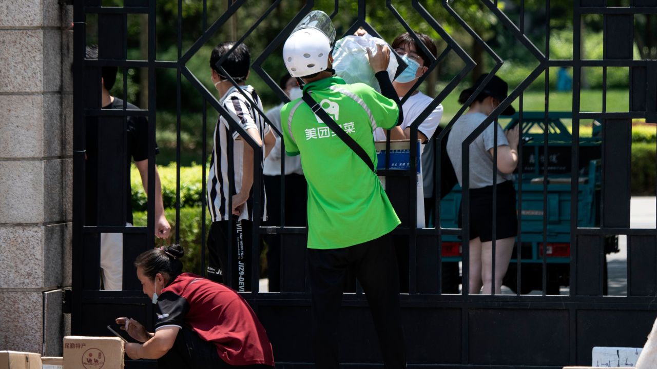 A delivery worker hands over items ordered online by a resident living in a compound under lockdown in Beijing.