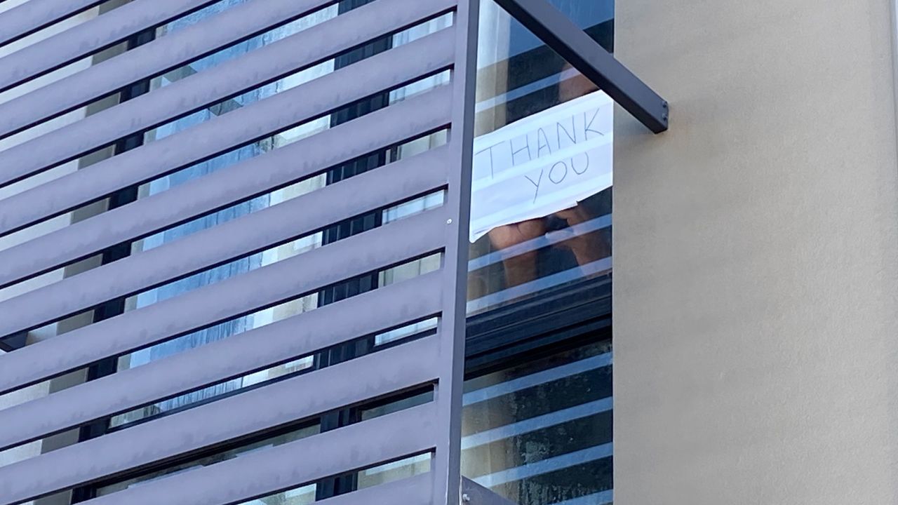 A detainee holds a sign to the window of his Kangaroo Point hotel room: "Thank you."