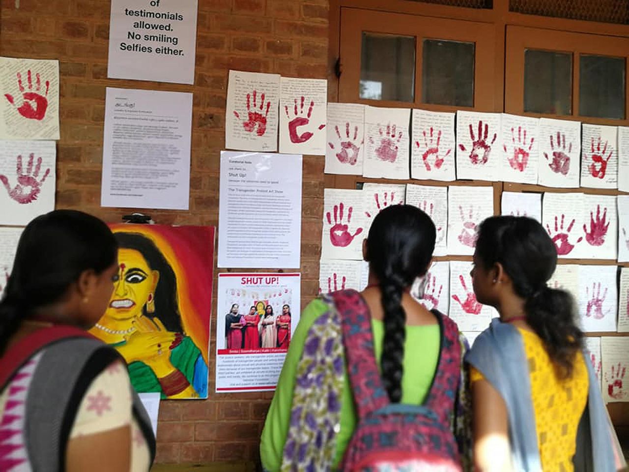 Students read Red Wall testimonials. Kalki sees the red painted palms signifying "a slap against abusers and a sign of resistance." Exhibited together, she says the palms are a unified and powerful statement from victims seeking justice for the crimes committed against them. 