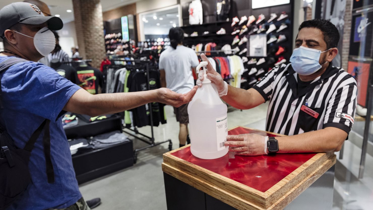 A worker in a protective mask at the entrance to a Foot Locker store in San Francisco, California, gives a shopper hand sanitizer on Thursday.