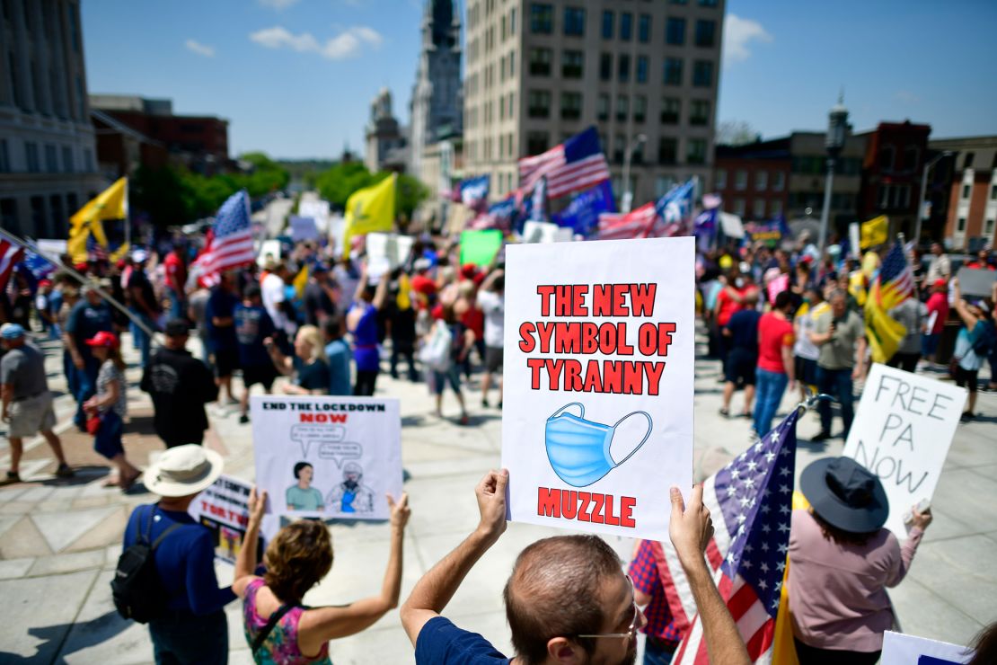 A demonstrator holds a placard with a face mask stating "THE NEW SYMBOL OF TYRANNY MUZZLE" rallying outside the Pennsylvania Capitol Building to protest the continued closure of businesses due to the coronavirus pandemic on May 15, 2020 in Harrisburg, Pennsylvania.