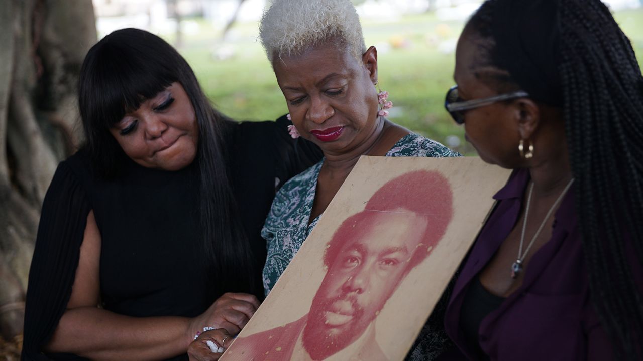 LoLisa Miller-Bradford, Roz Miller-Lloyd and Vallorie Miller hold a photo of their father Arthur Miller at the cemetery where he is buried.