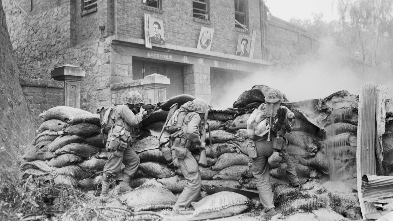 US Marines take cover behind a barricade as street fighting rages in Pyongyang. On the wall in the background are images of Soviet leader Joseph Stalin and North Korean leader Kim Il Sung.