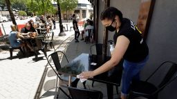 Jayda Boykin, of Norwood, Mass., a worker at Lewis' Bar and Grille, cleans a table and chairs, Thursday, June 18, 2020, in an outdoor dining area on a sidewalk at the restaurant, in Norwood, Mass. Restaurants in Massachusetts began offering outdoor dining, with the restriction that tables be placed at least six feet apart, as part of phase 2 of the state's reopening during the coronavirus pandemic. (AP Photo/Steven Senne)