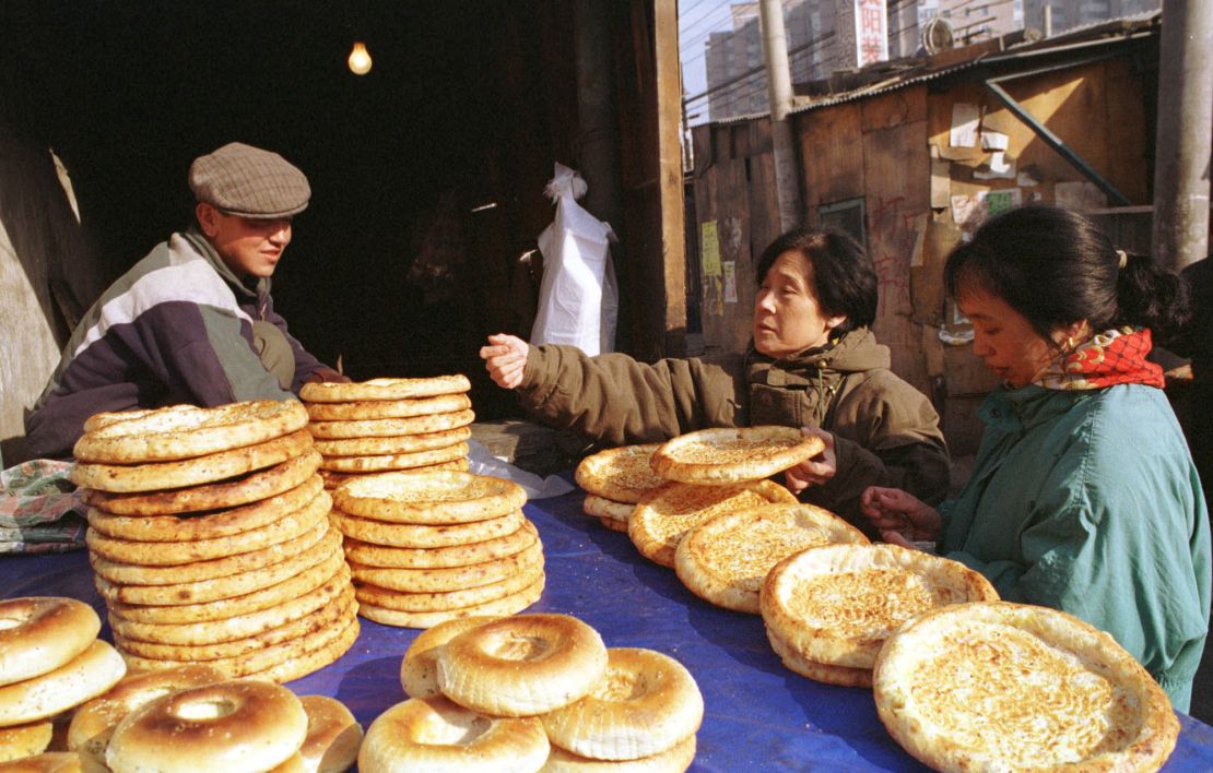 A Uyghur man sells traditional flat bread to women shoppers along Beijing's Xinjiang Street in 1999.