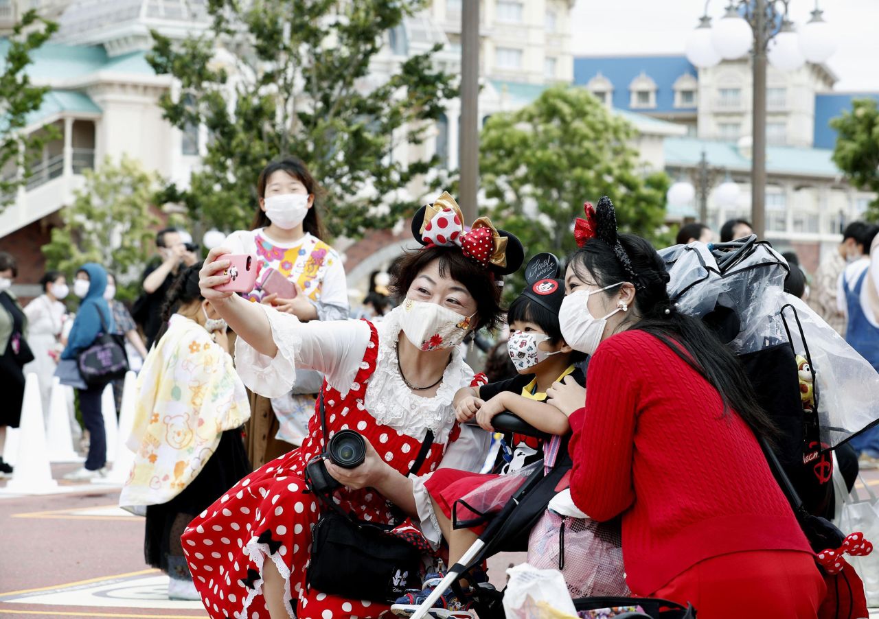 People wearing face masks to protect against the spread of the new coronavirus take a selfie together before they wait to enter Tokyo Disneyland on Wednesday, July 1.